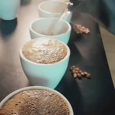 Hot water being poured over the cupping bowls to break the crust